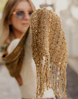 Model in the background holding the golden textured handwoven scarf. Close-up of the eyelash fringe.