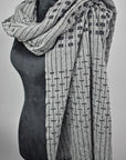 This women's handwoven gray shawl draped on a black mannequin showcasing it's design.