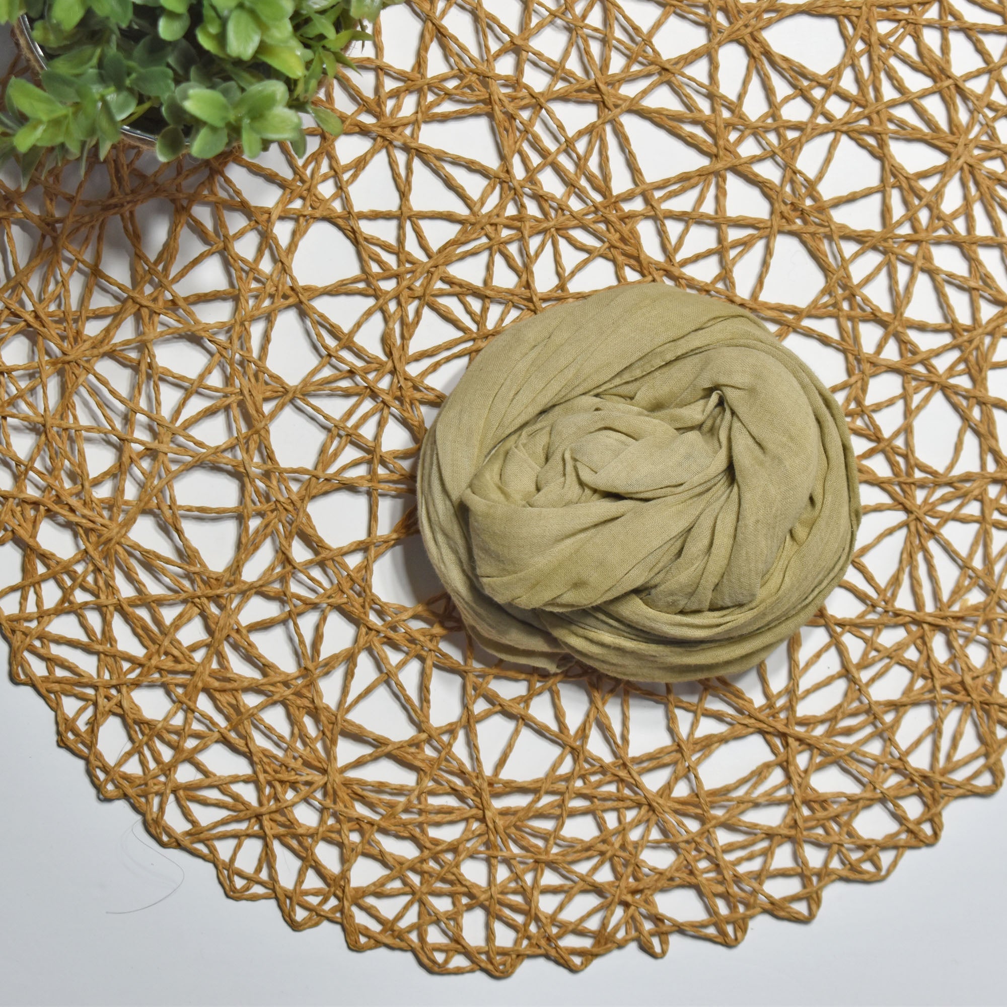 Green tea hand-painted scarf on a white table with a plant and rattan doily
