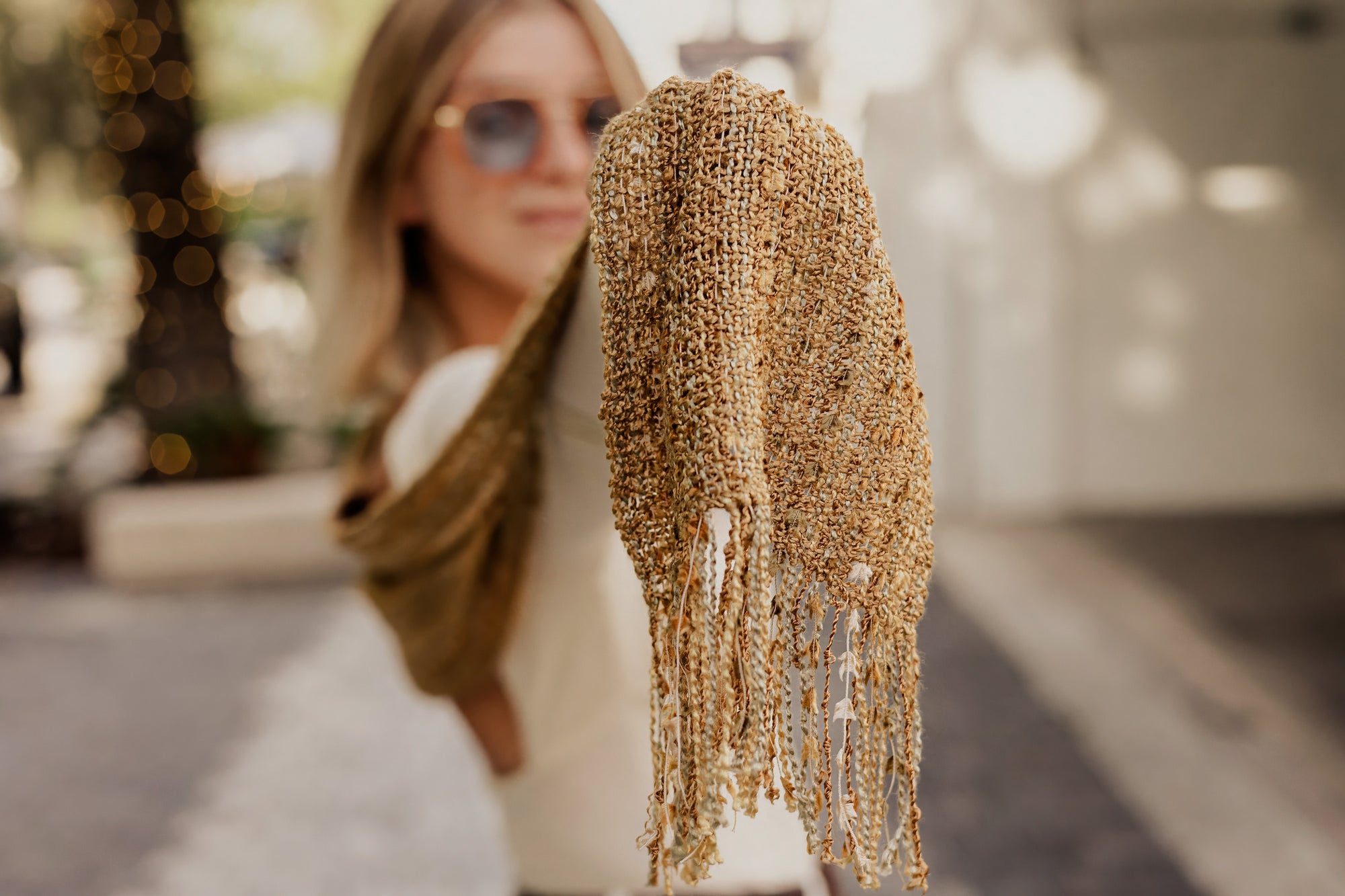 Model in the background holding the golden textured handwoven  scarf. Close-up of the eyelash fringe.