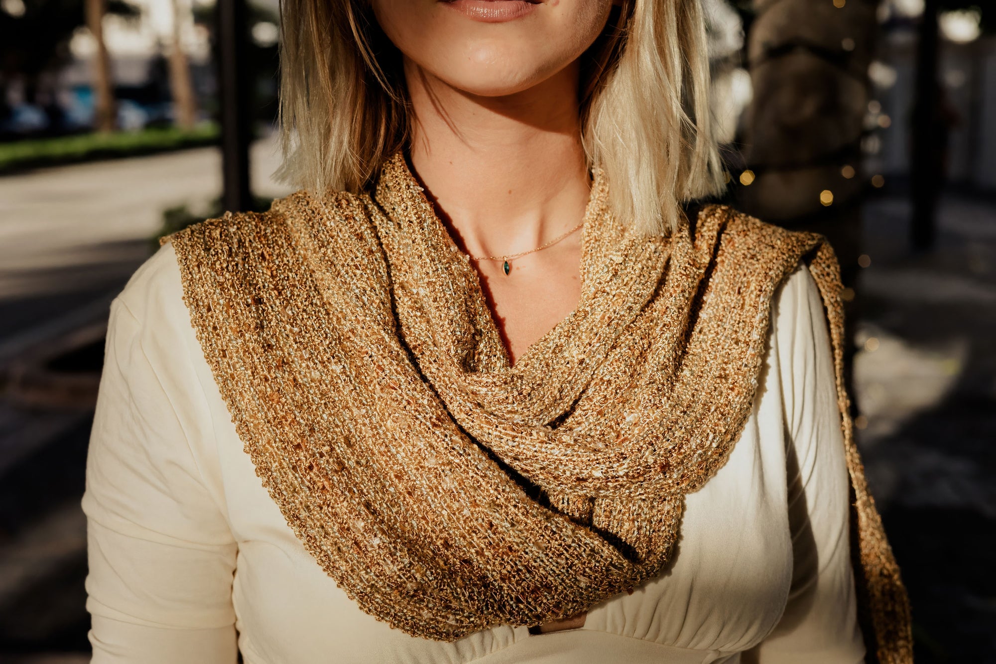 Model wearing the handwoven scarf with blurred trees and a street in the background