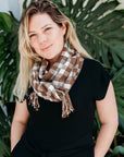 Chestnut brown + white handwoven wool scarf wrapped on a model. The model is standing in from of a tree.