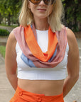 Apricot + blue handwoven scarf modeled on a woman wearing a white crop top and apricot skirt. She is standing on the sidewalk and wearing sunglasses.