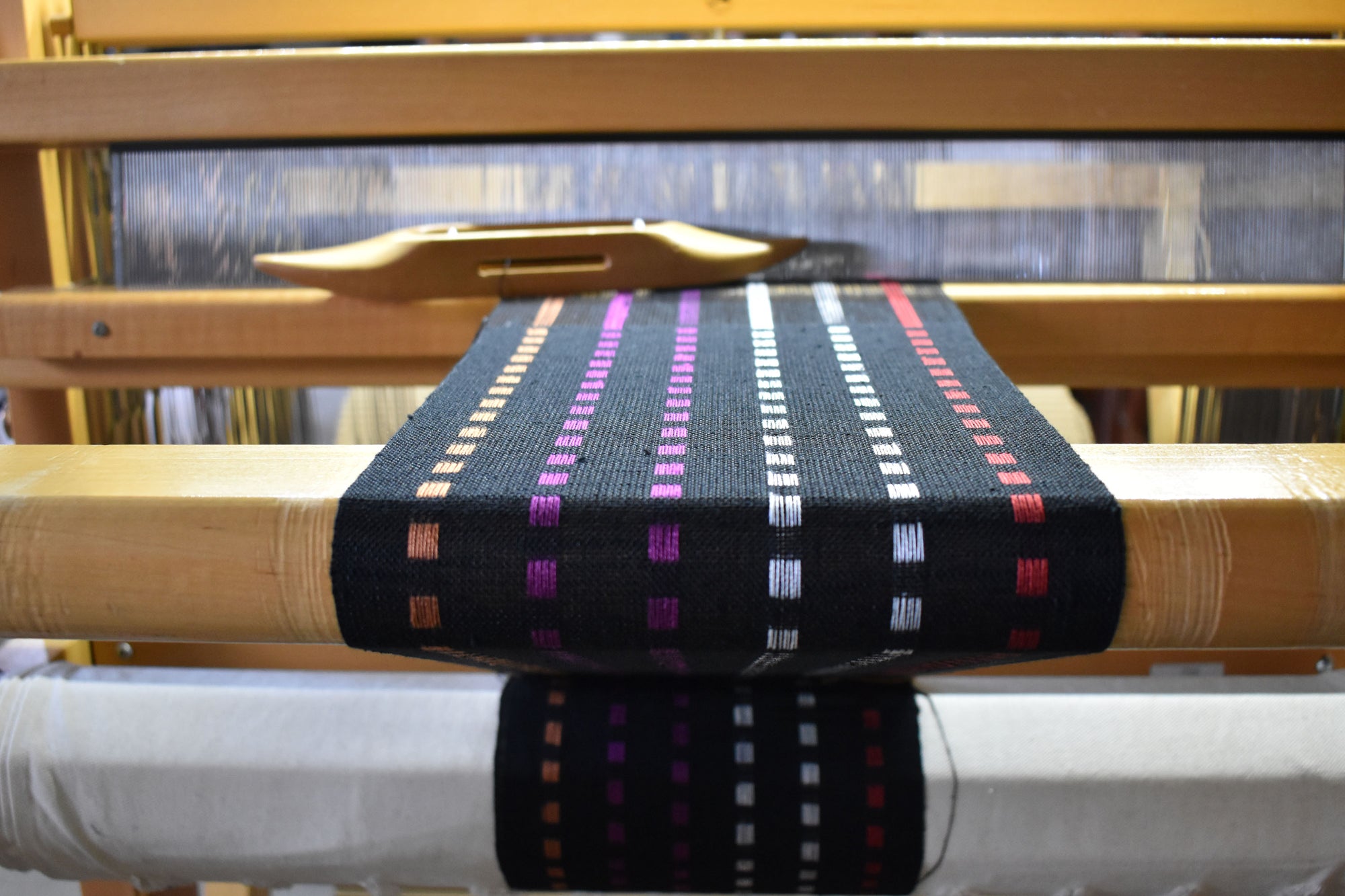 The black sunset scarf woven on a floor loom with a shuttle in view