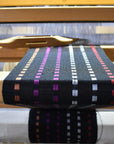 The black sunset scarf woven on a floor loom with a shuttle in view