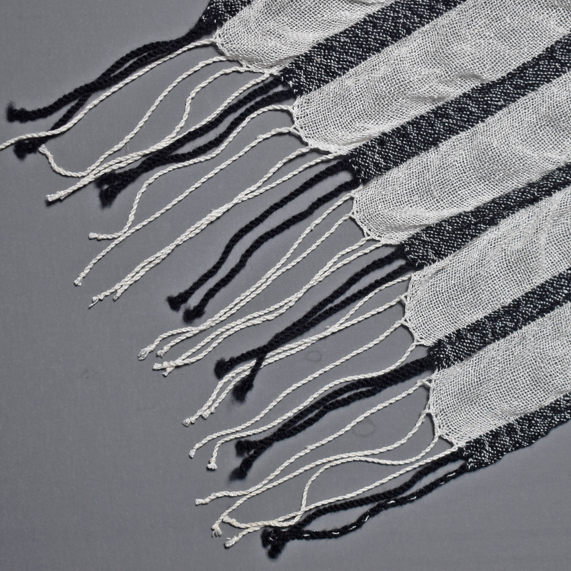 Close-up of the hand twisted fringe on the black and white striped handwoven scarf