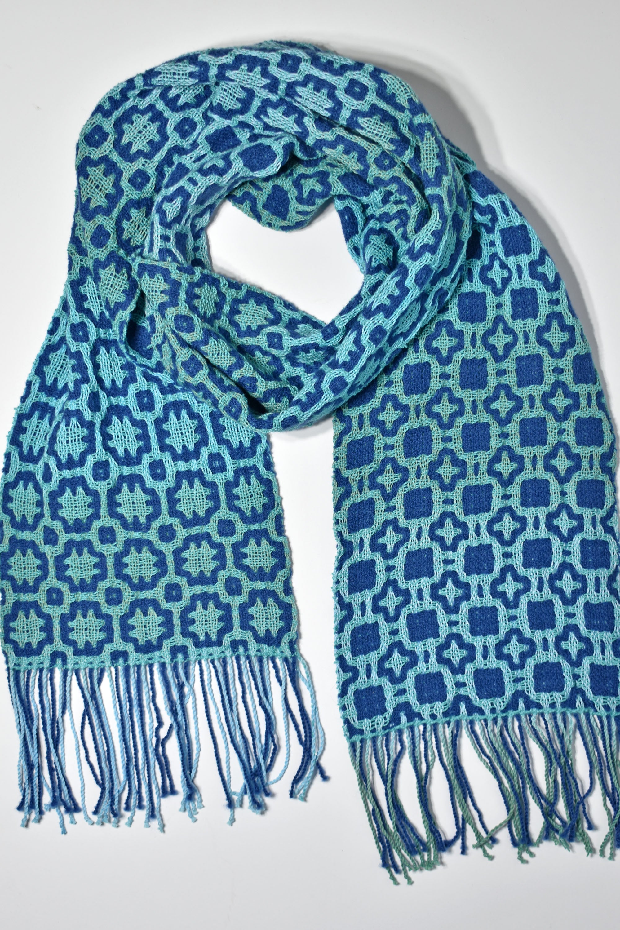 Blue + green handmade scarf styled on a white table. Check out the different designs on the front and back