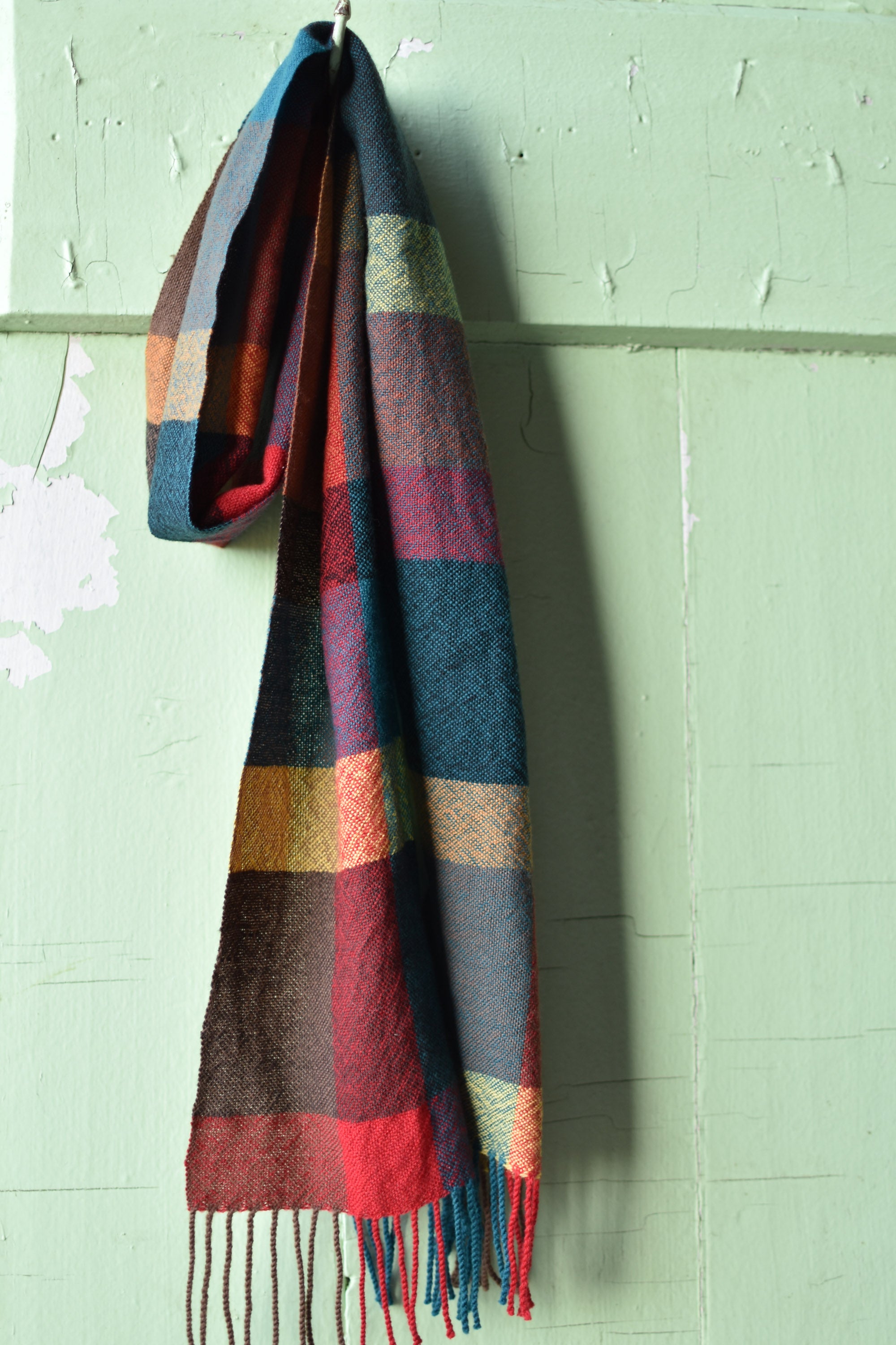 Handwoven merino wool scarf draped over a hook on a old farmhouse door