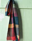 Handwoven merino wool scarf draped over a hook on a old farmhouse door