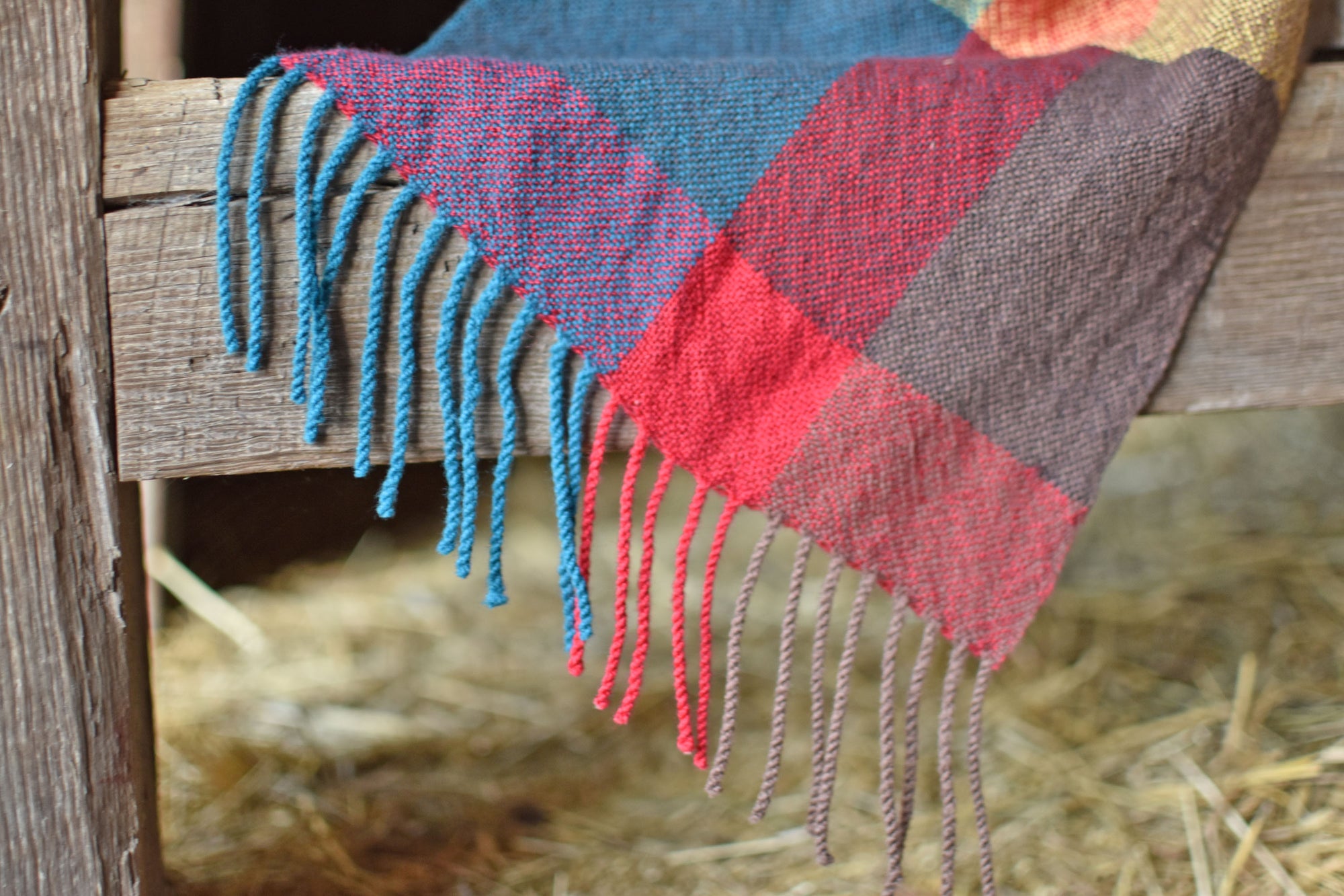 Close-up of the hand twisted fringe on the bright colored handwoven merino wool scarf on a barn ladder