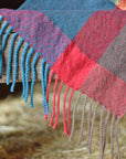 Close-up of the hand twisted fringe on the bright colored handwoven merino wool scarf on a barn ladder