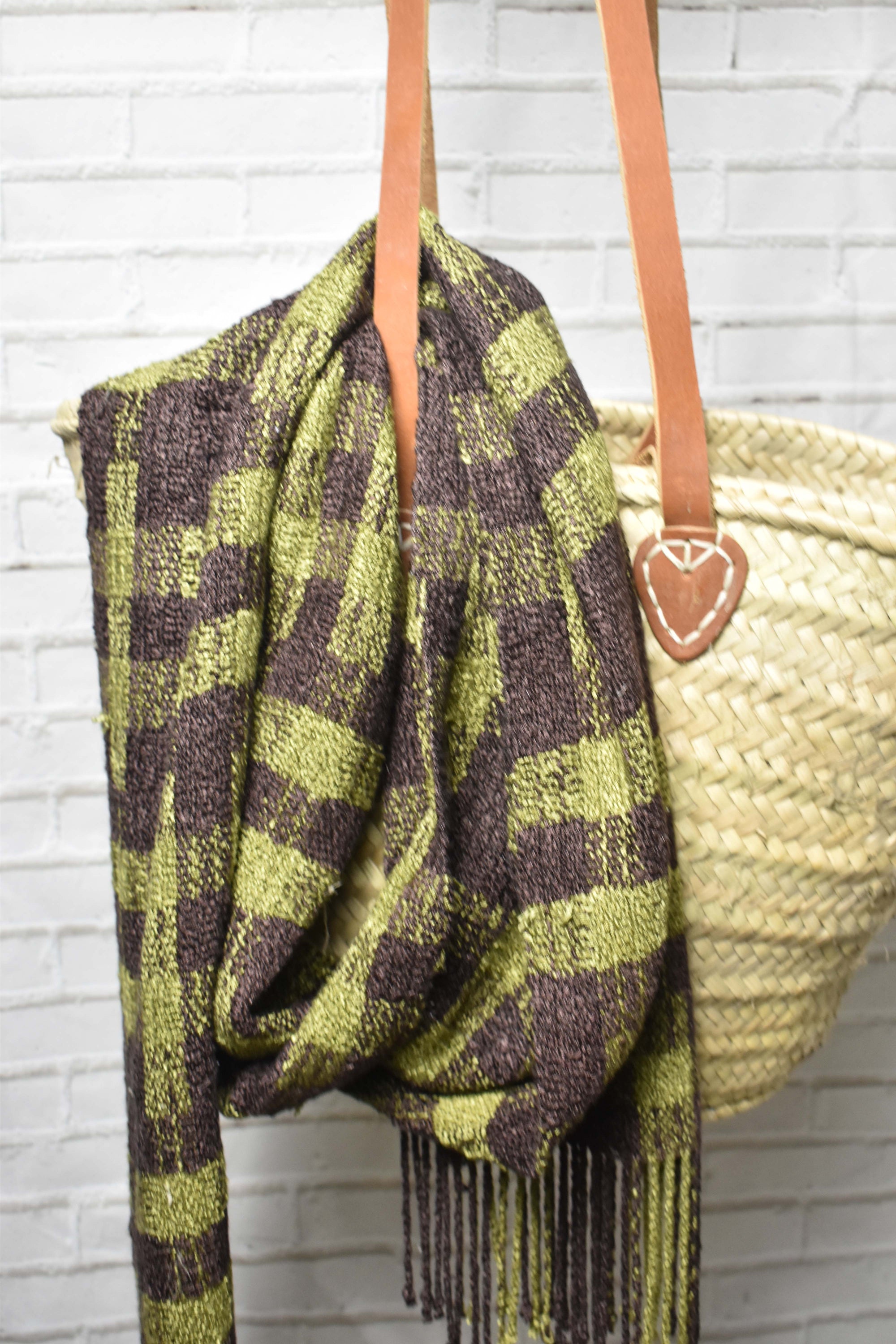 Brown + green handwoven scarf draped over a bag with a brick wall in the background