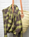 Brown + green handwoven scarf draped over a bag with a brick wall in the background