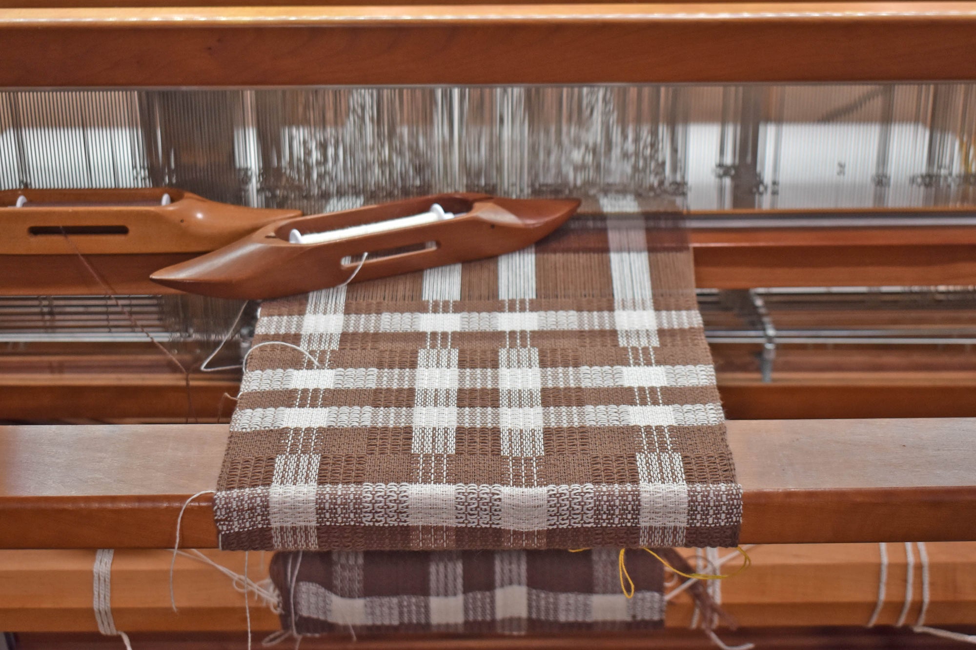 Chestnut brown + white scarf being handwoven on a wooden floor loom