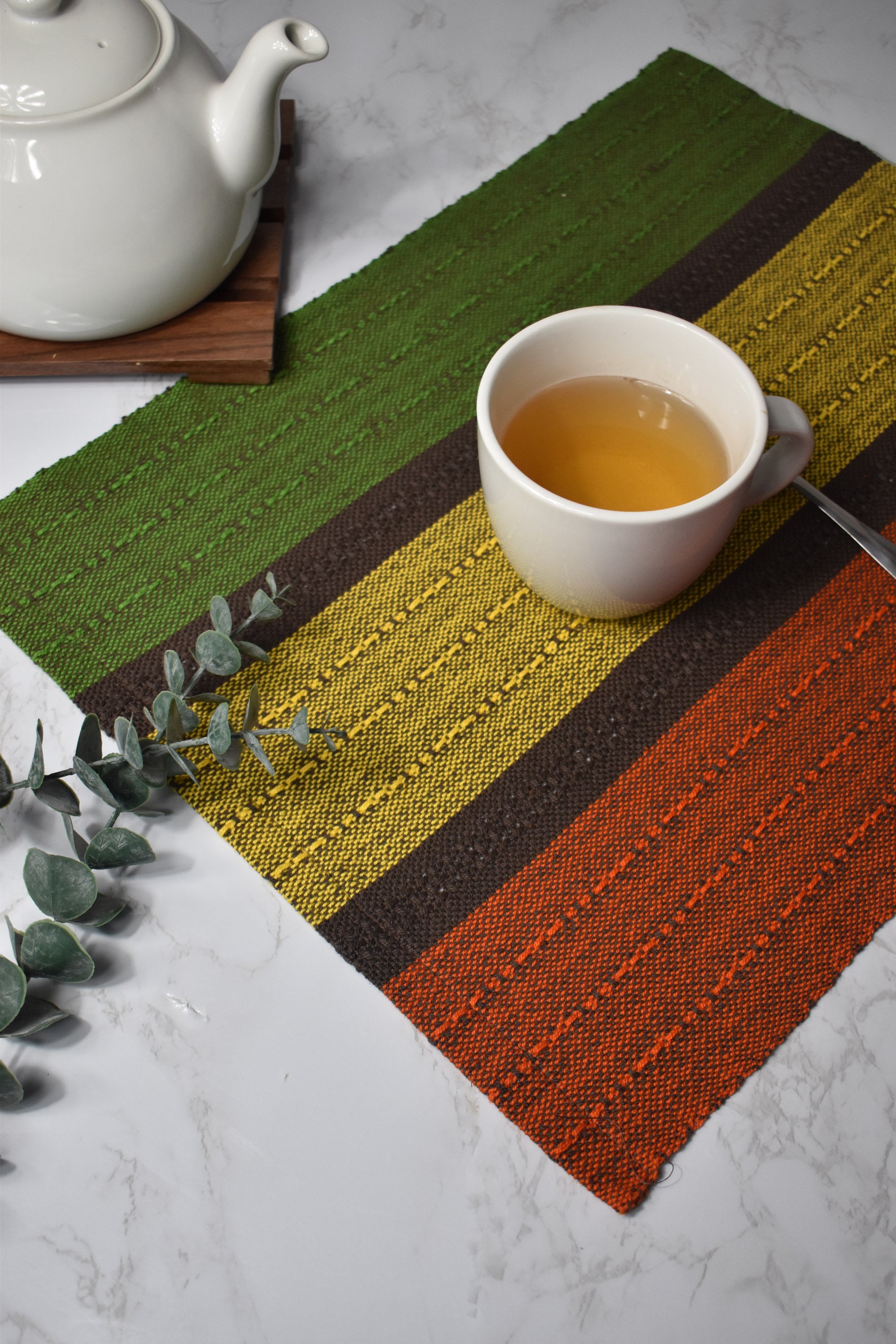 Fall inspired handwoven placemat with a cup of tea on top of it. There&#39;s a tea pot and some eucalyptus in the photo as well