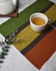 Fall inspired handwoven placemat with a cup of tea on top of it. There's a tea pot and some eucalyptus in the photo as well