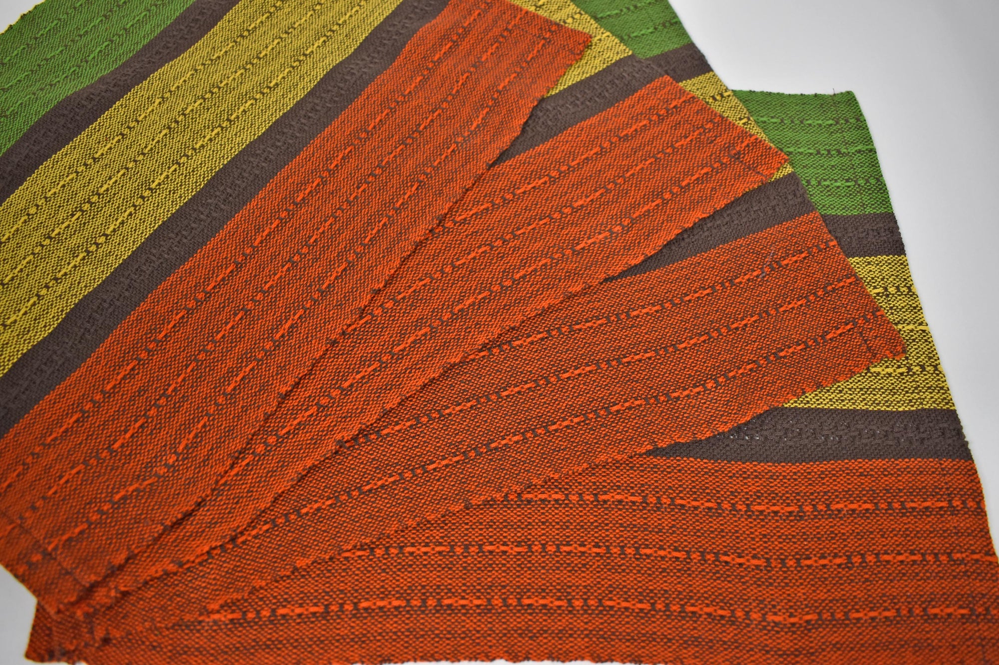 Four fall inspired handwoven placemats arranged on a white table