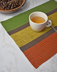 Fall inspired placemat on a marble table with a cup of tea on top of it. Bowl of pine cones on the top left of photo.