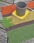 Handwoven fall placemat sitting on a picnic table. There are green leaves and mug in view.