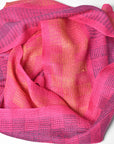 Fuchsia scarf laying on a white table. Enjoy the bright pinks, orange, and purple colors.