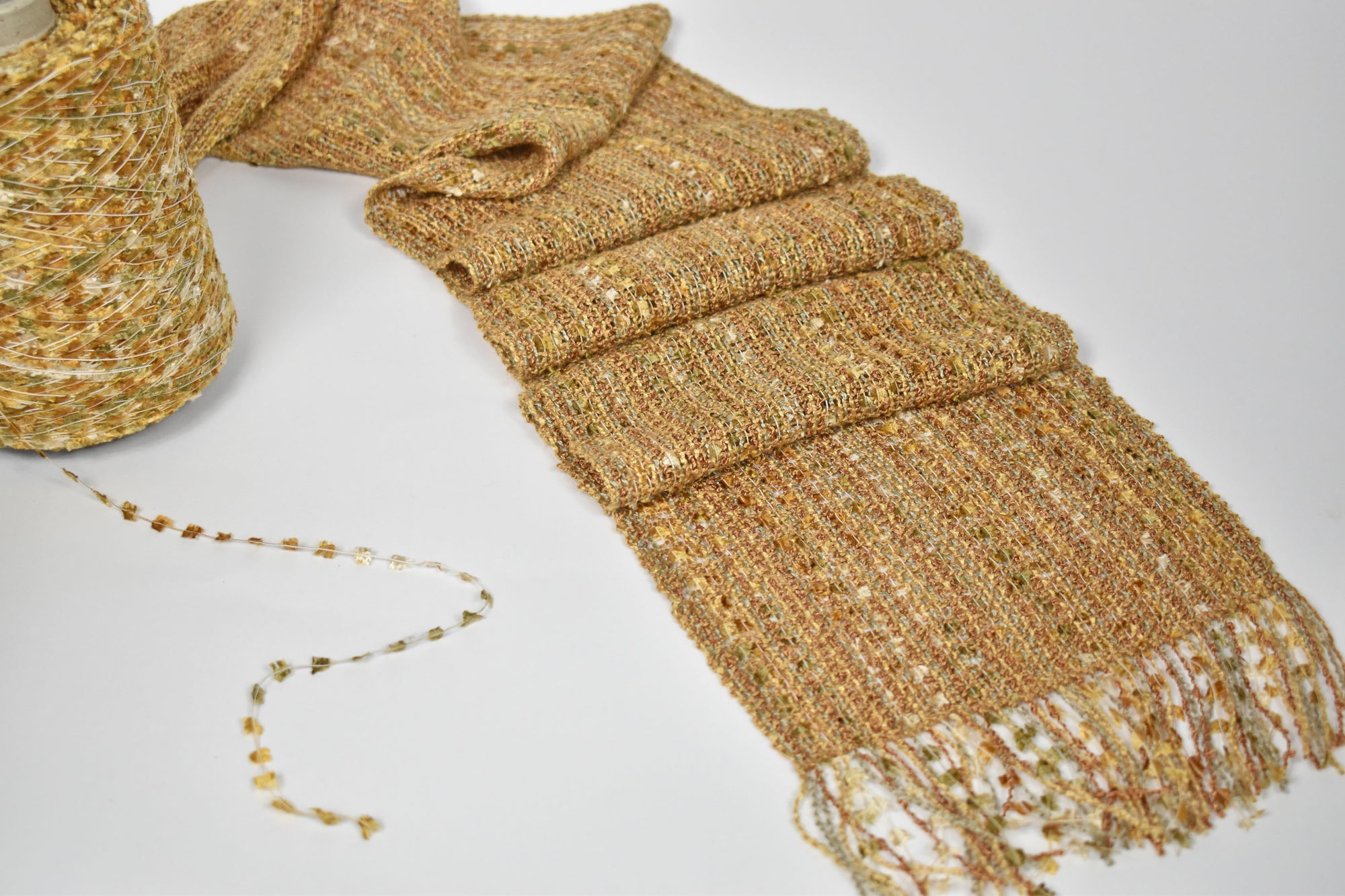 Golden textured scarf laying on a table with a cone of one of the textured yarns