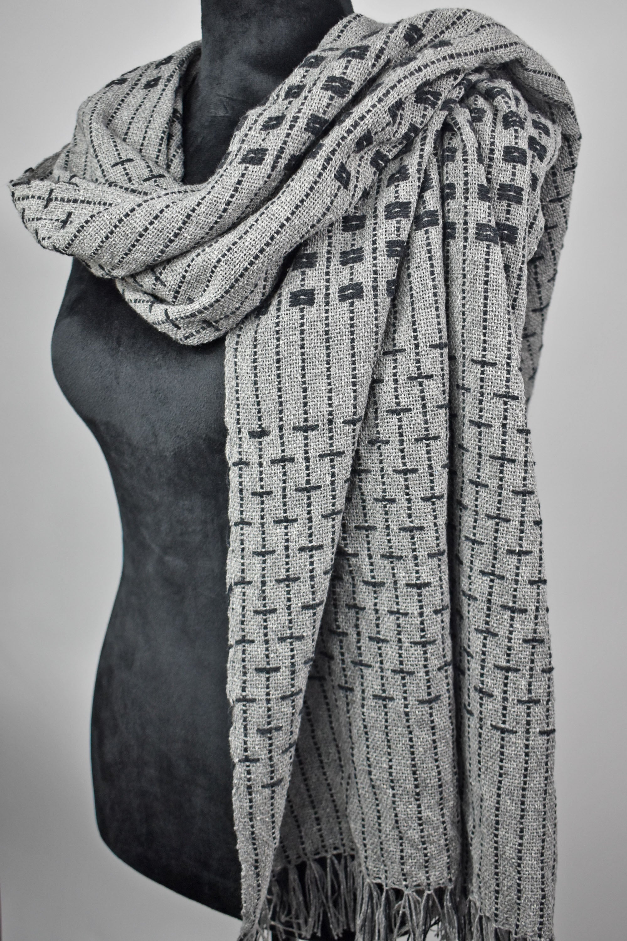 This women's handwoven gray shawl draped on a black mannequin showcasing it's design.