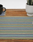 Striped placemat on a wooden table. Silverware is on top of the placemat. A mug and a plant is also in view.