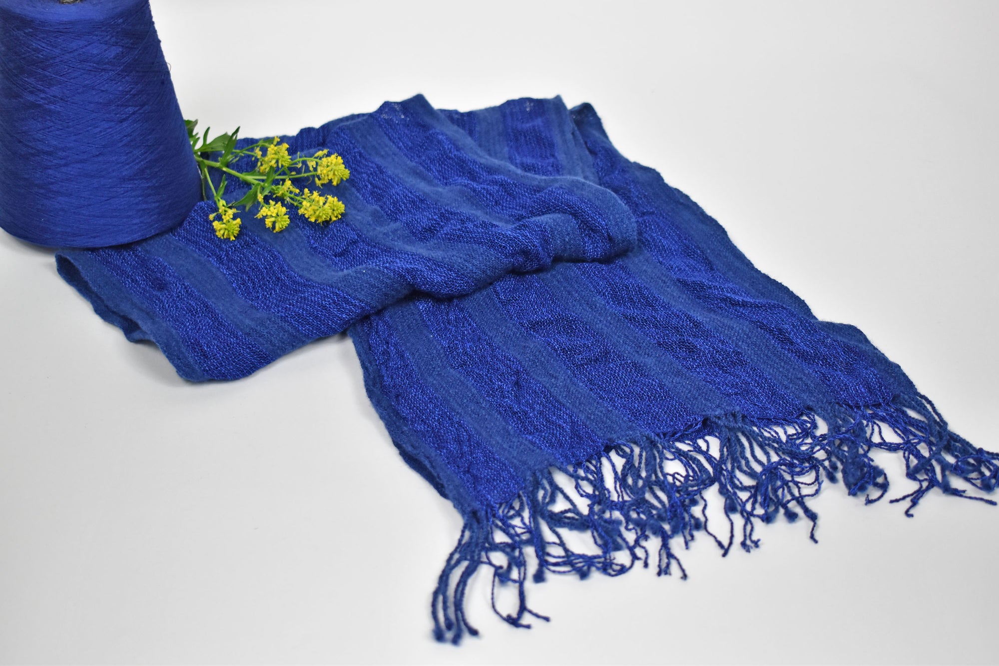 Blue scarf folded on a table with the yarn used to weave the scarf and yellow flowers