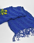 Blue scarf folded on a table with the yarn used to weave the scarf and yellow flowers