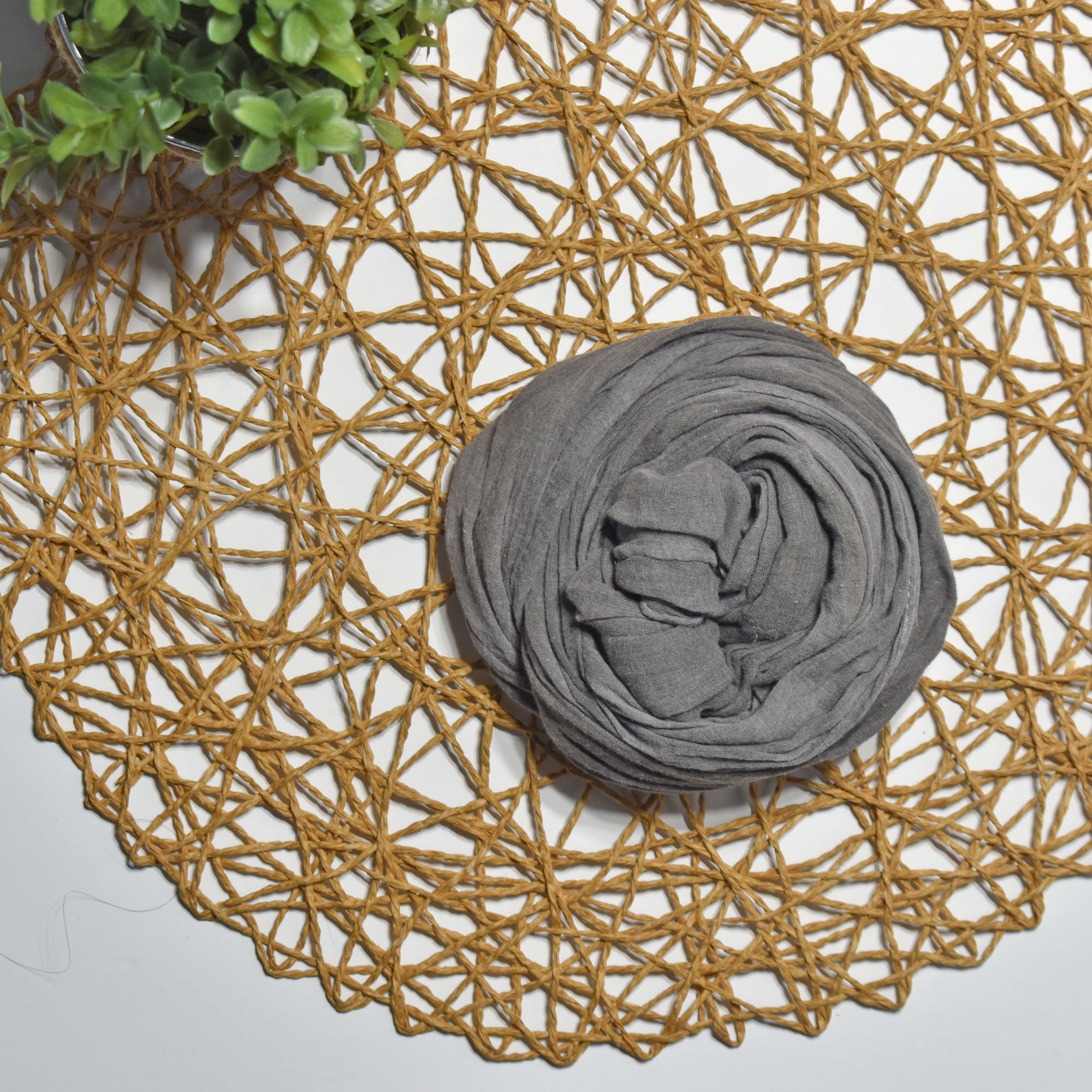 Charcoal gray hand-painted scarf on a white table with a plant and rattan doily