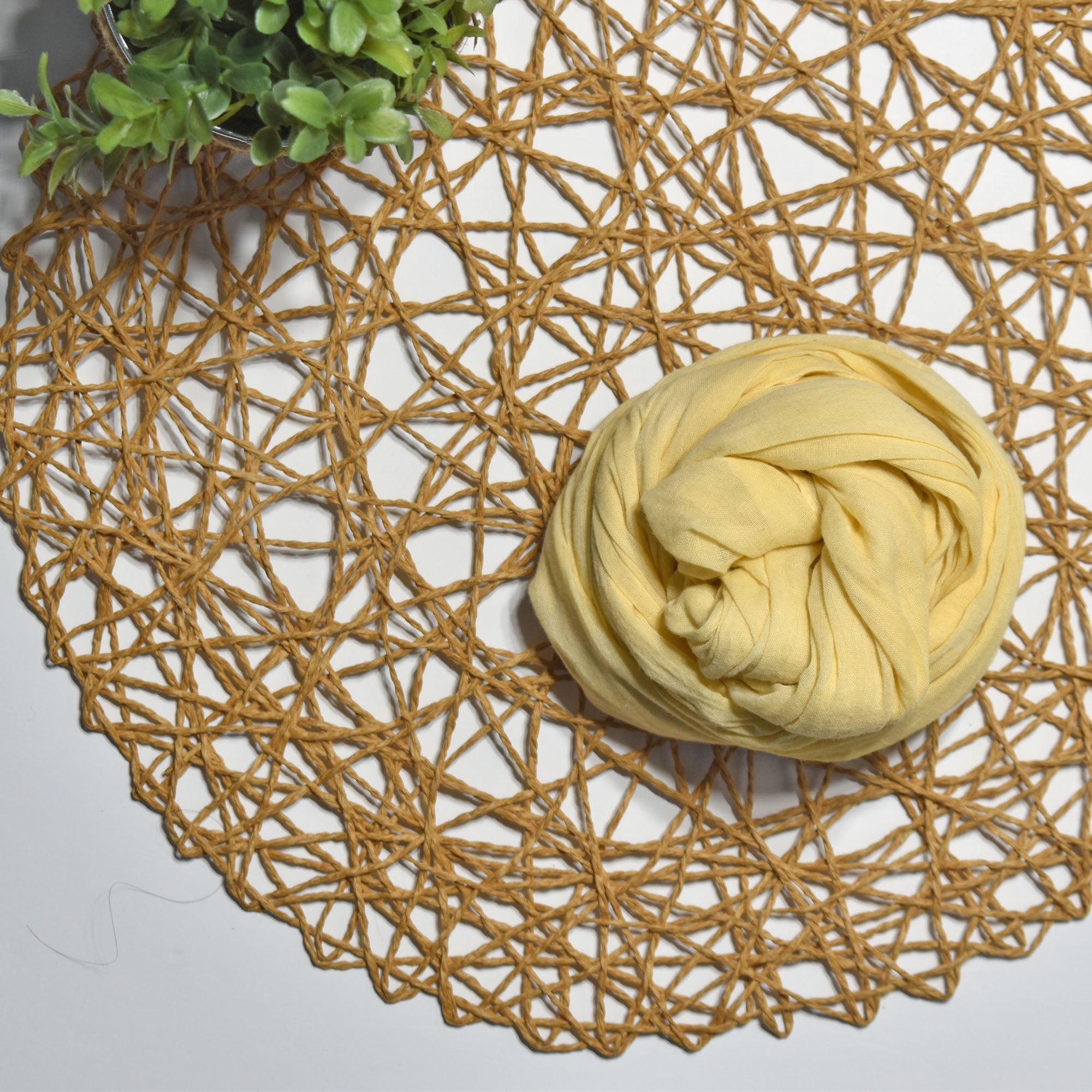 Golden yellow hand-painted scarf on a white table with a plant and rattan doily