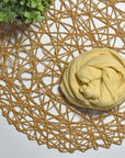 Golden yellow hand-painted scarf on a white table with a plant and rattan doily