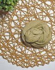 Green tea hand-painted scarf on a white table with a plant and rattan doily