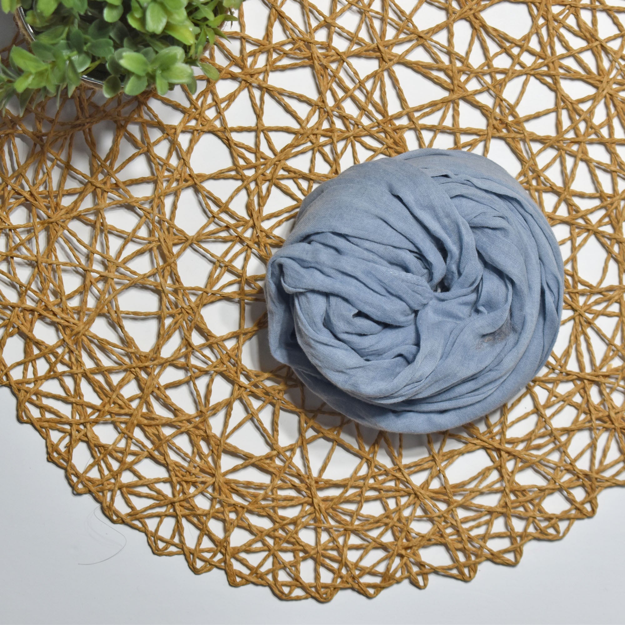 Sky color hand-painted scarf on a white table with a plant and rattan doily