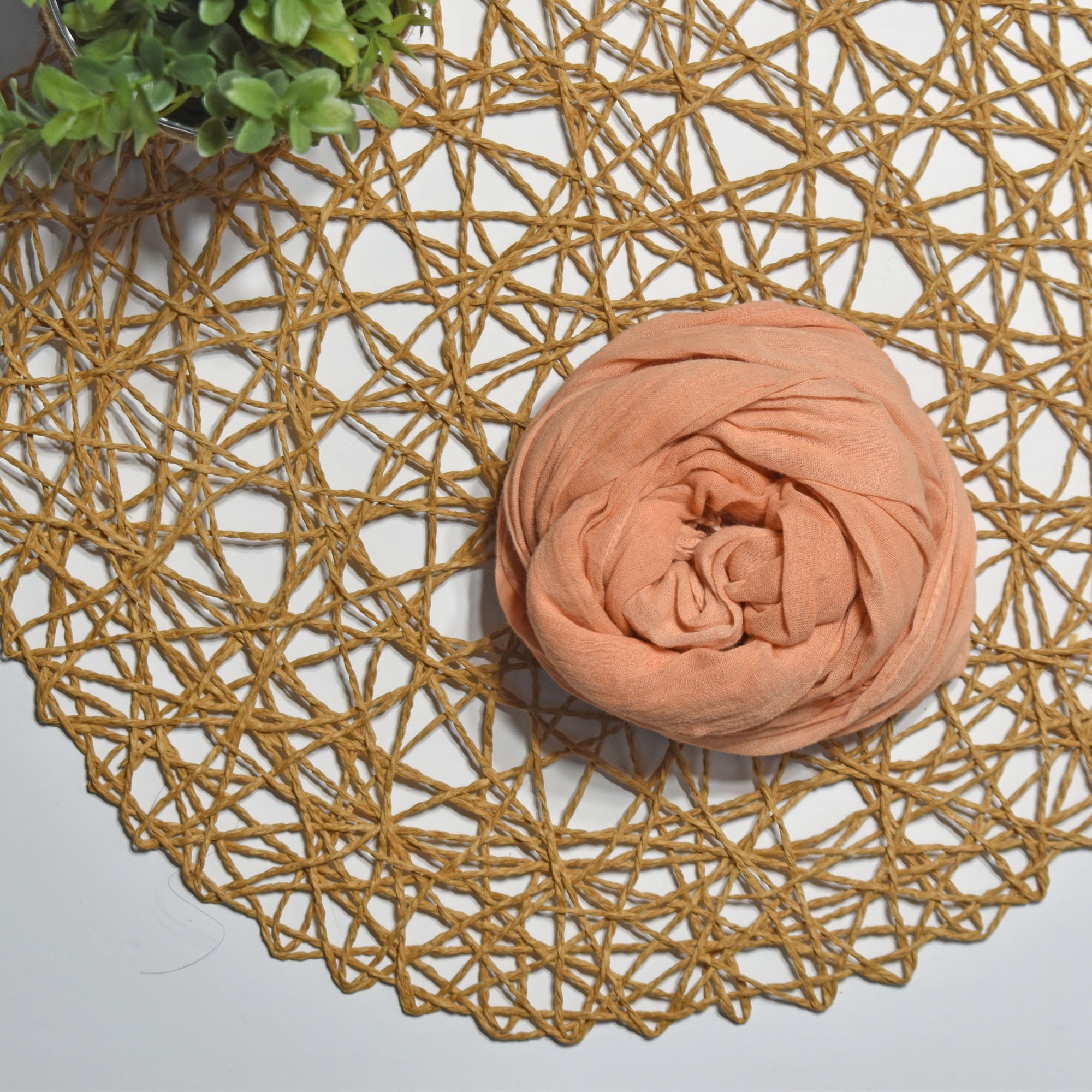 Terra cotta color hand-painted scarf on a white table with a plant and rattan doily