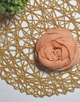 Terra cotta color hand-painted scarf on a white table with a plant and rattan doily