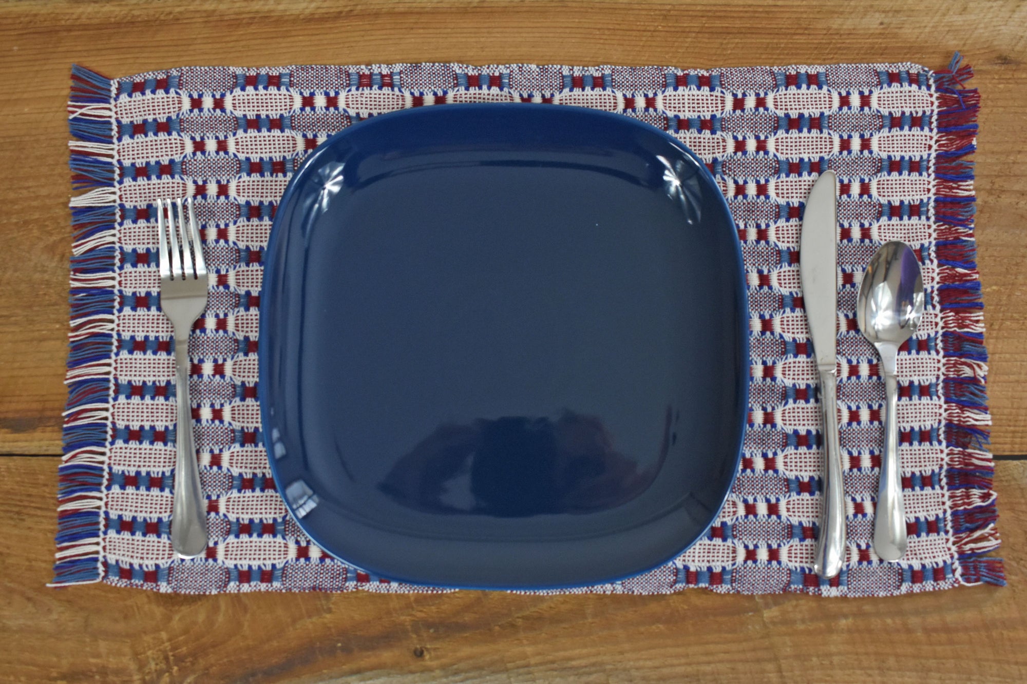 Patriotic placemat on a wooden table with a blue plate and silverware on top.