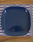 Patriotic placemat on a wooden table with a blue plate and silverware on top.