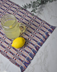 Patriotic handwoven organic cotton placemat on a white table. A lemon and a glass of lemonade on top of the placemat. Eucalyptus in view.