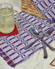 Patriotic placemat on top of a blanket with a picnic basket, glass of lemonade, silverware, and a book