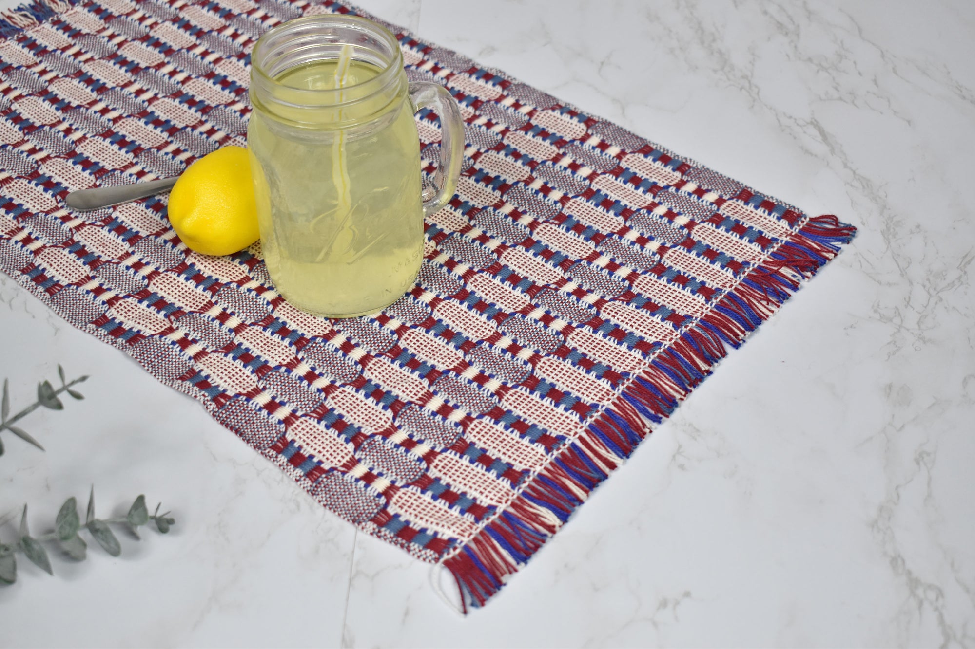 Patriotic placemat on a white table with a lemon and a glass of lemonade on top. Eucalyptus is view.