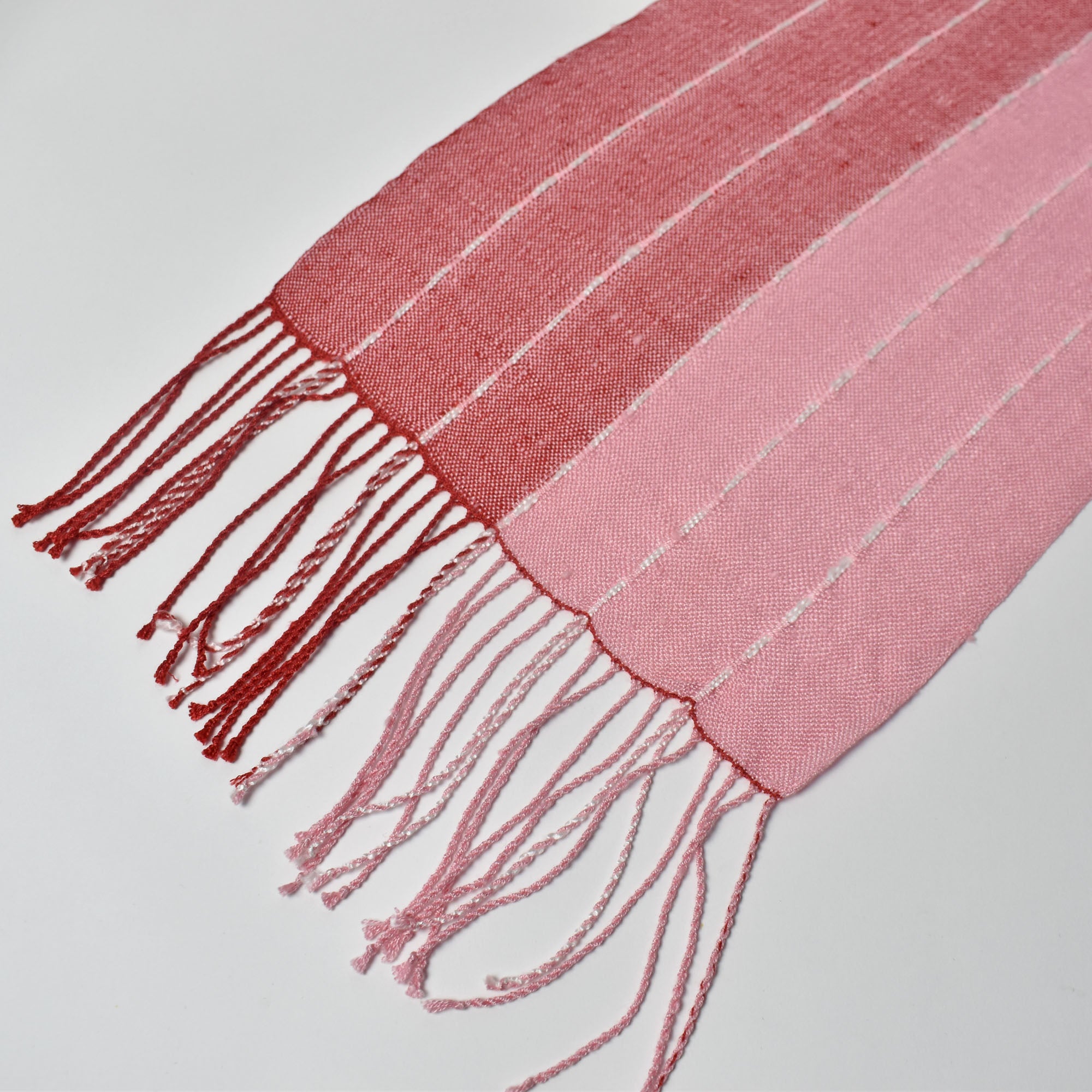 Close-up of the hand twisted fringes on the pink + red handwoven scarf