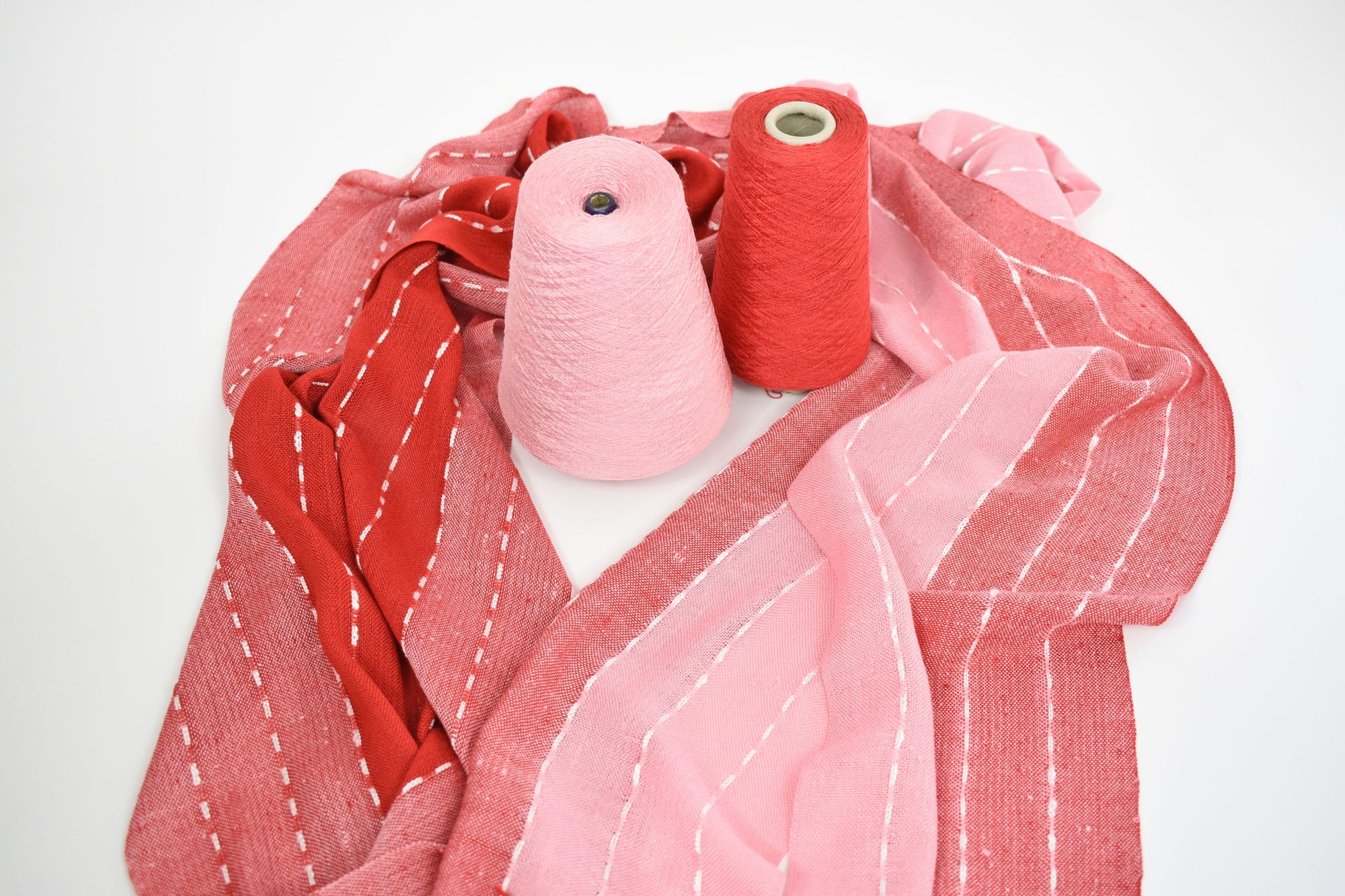 Pink + red scarf draped on a white table with the red and pink cones of yarns