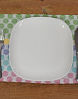 The polka dot placemat is laying on a wooden table. There's a white plate and silverware on top of the placemat.