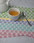 Several polka dot placemats on a white table. A cup of tea, spoon, and tea pot are also in view.