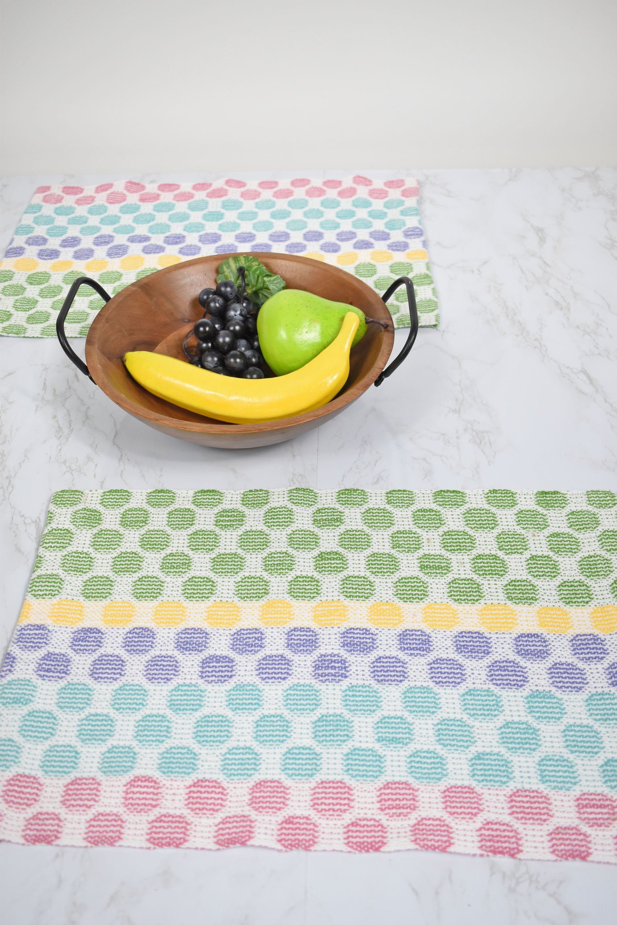 Two polka dot placemats on a white table with a fruit basket in the center of the table