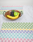 Two polka dot placemats on a white table with a fruit basket in the center of the table