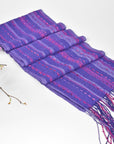 Handwoven purple scarf displayed on a white table with some purple flowers