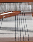 White handwoven merino scarf being created on a wooden floor loom. 