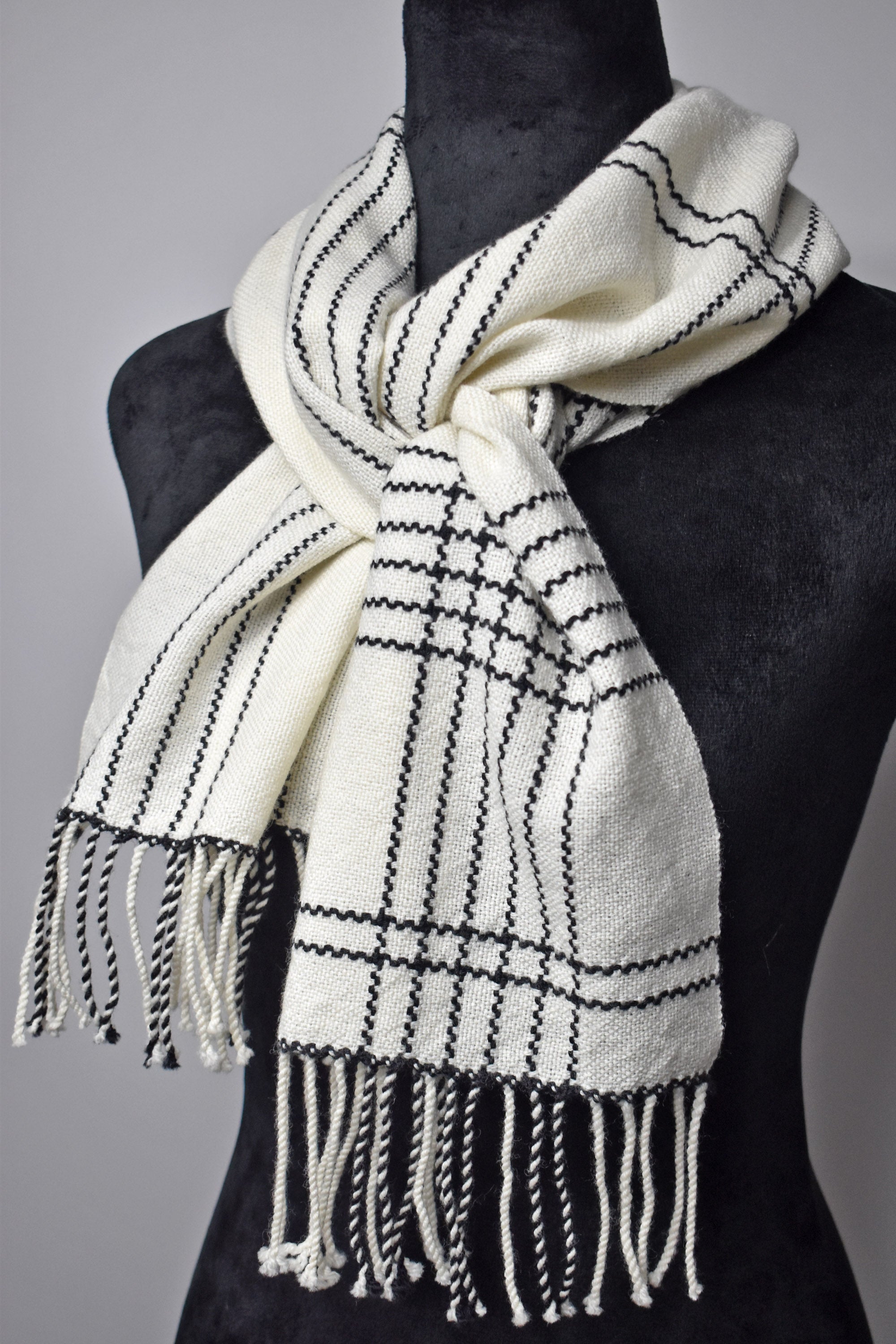 White handwoven merino scarf with black accents on a mannequin